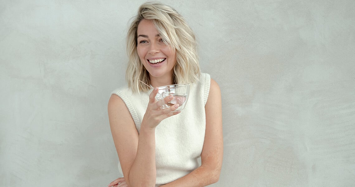 Mujer rubia sonriendo con un vaso en la mano