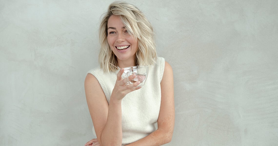Mujer rubia sonriendo con un vaso en la mano