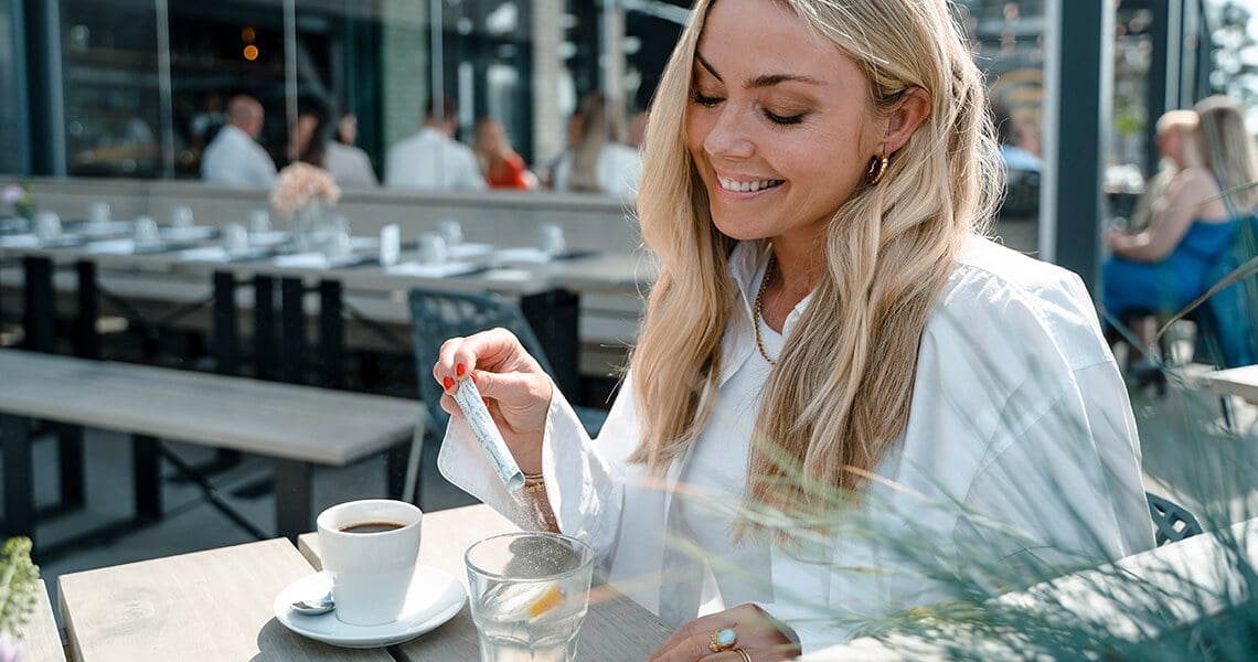 Mujer rubia con camisa blanca mezclando The Solution en el café