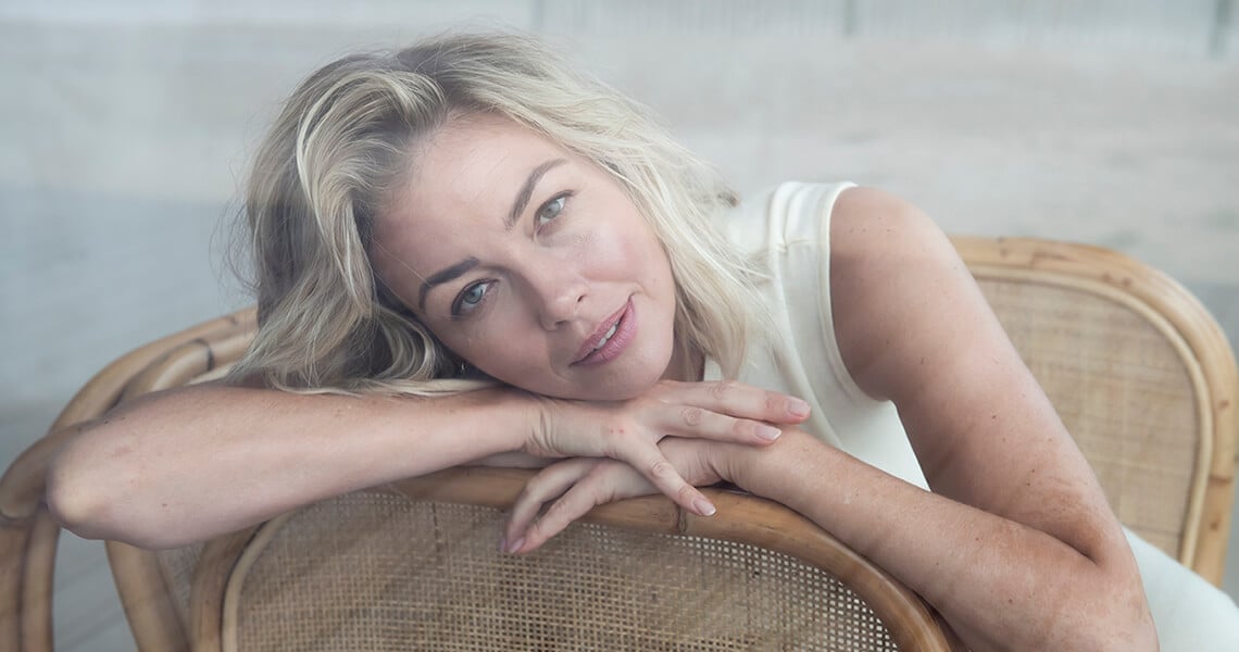 Mujer rubia sentada en un sillón mirando a cámara