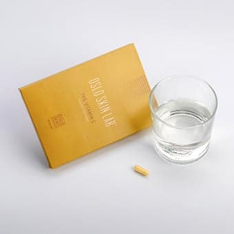Envase de Vitamina C junto a un vaso de agua